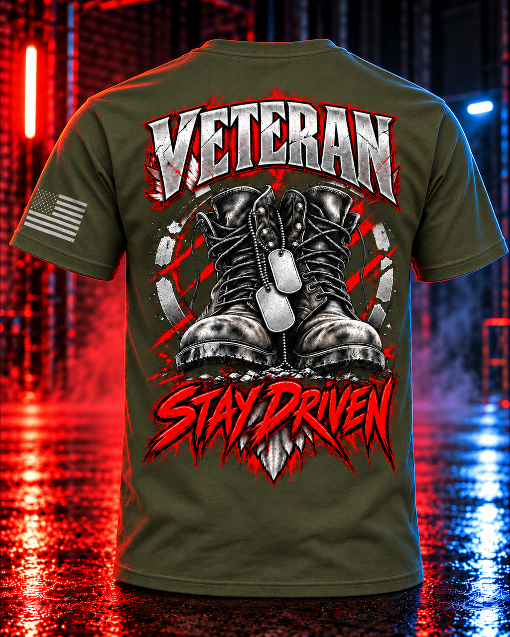 An olive green t-shirt shown from the back, featuring a large graphic print with the words 'VETERAN' and 'STAY DRIVEN' in red and white, flanking a graphic of black combat boots and dog tags. The shirt is displayed against a dark, wet street background illuminated by red and blue neon lights.